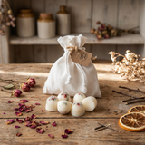 Beauty Scents Six wax melts with red pepper and greens, with a white linen bag behind them, surrounded by rose petals and dried orange slices on a wooden table in a cozy workshop.