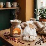 Beauty Scents Six wax melts with red pepper and greens, with a white linen bag behind them next to an oil burner, surrounded by rose petals and dried orange slices on a wooden table in a cozy kitchen.