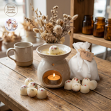 Beauty Scents Eleven loose wax melts with red pepper and greens on a wooden table, beside an oil burner with one wax melt melting on the top tray, and a white linen bag nearby.