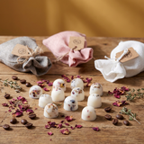 Beauty Scents Three linen bags of wax melts in grey, pink, and white, with loose wax melts and rose petals in front.