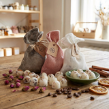 Beauty Scents Loose wax melts with rose petals on a wooden table, next to a small plate of wax melts, with three linen bags in grey, pink, and white in the background.