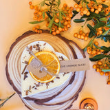 Small heart-shaped orange and cinnamon scented candle decorated with shredded cinnamon sticks on white soy wax background
