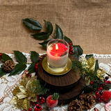 Decorative candle on a wooden stand with green leaves, red berries, and pine cones on a lace tablecloth.