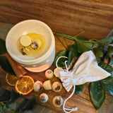Beauty Scents orange and cinnamon scented wax melts with shredded cinnamon sticks, seven loose on a wooden table next to an oil burner melting two wax melts and a white linen bag.