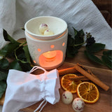 Beauty Scents Rose Petal wax melts setup with two loose wax melts on a wooden table next to a white linen bag and an oil burner melting two melts.