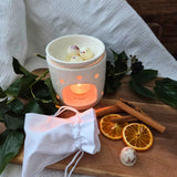 Beauty Scents wax melts with shredded cinnamon, two melts melting in an oil burner next to a white linen bag, angled lower view.