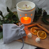 Two Beauty Scents wax melts with shredded cinnamon on a table next to a grey linen bag and an oil burner melting three melts.
