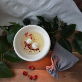 Beauty Scents wax melts with rose petals, two melts melting in an oil burner next to a grey linen bag, top view.