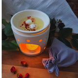 Beauty Scents wax melts with rose petals, two melts melting in an oil burner next to a grey linen bag, angled view.