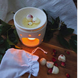 Beauty Scents wax melts with rose petals on a wooden table, some melting in an oil burner, others loose beside a white linen bag.