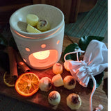 Beauty Scents wax melts setup with six loose wax melts on a wooden table next to a white linen bag and an oil burner melting three wax melts.