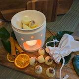 Beauty Scents wax melts, six loose on a wooden table beside a white linen bag and an oil burner with three wax melts melting.